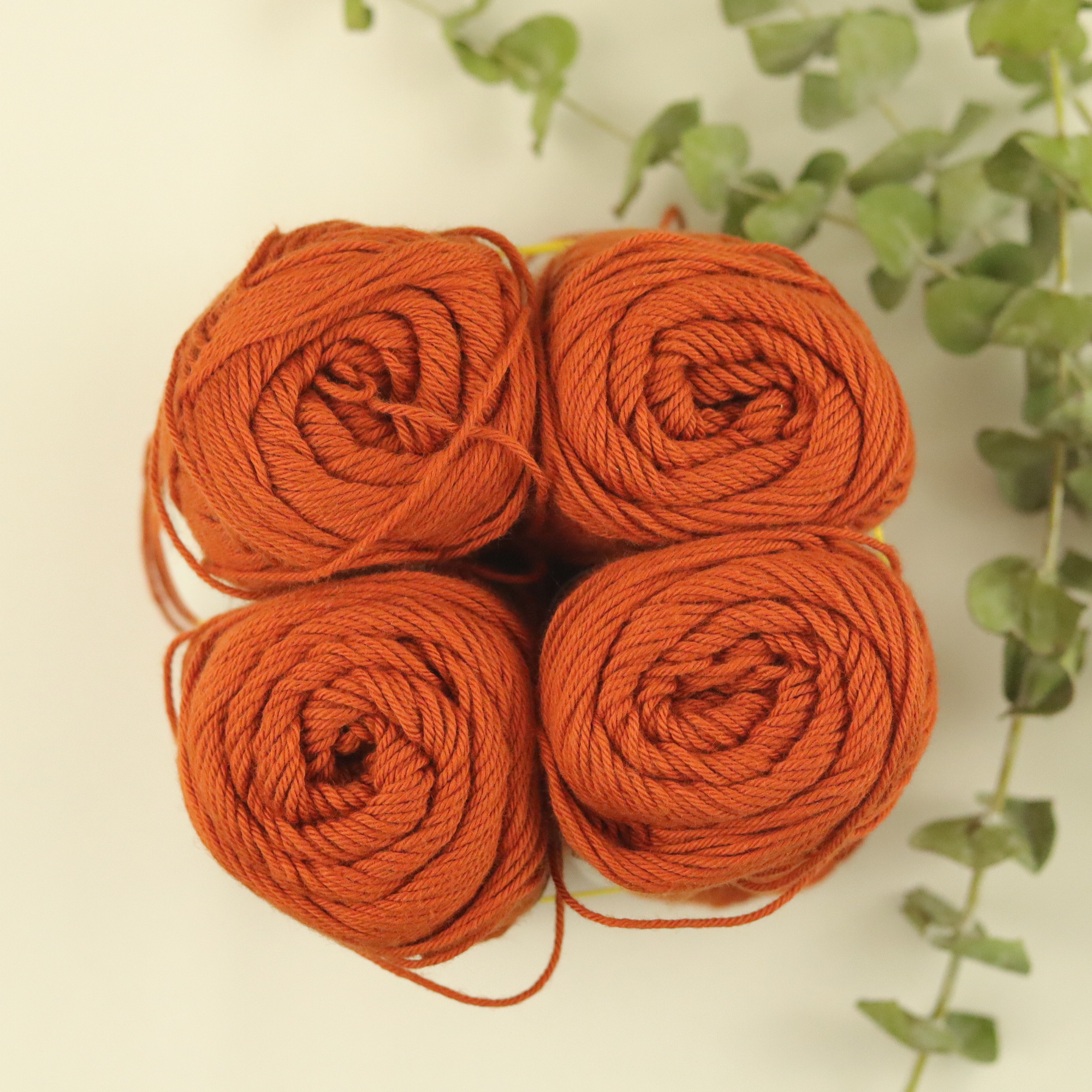 Four skeins of rust colored cotton yarn next to eucalyptus branches